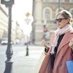 Elegant woman in a pink coat and sunglasses shopping with bags in a city street.